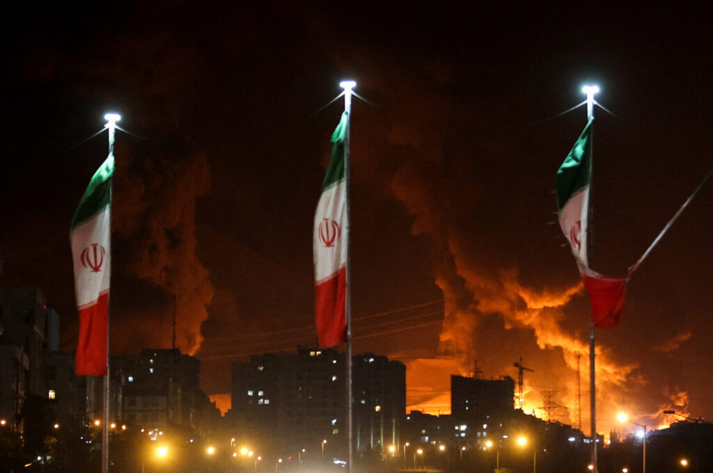 Banderas iraníes ondean mientras se eleva el fuego y el humo de un ataque israelí al depósito de petróleo de Sharan, tras los ataques israelíes contra Irán, en Teherán, Irán, el 15 de junio de 2025. Majid Asgaripour/WANA (Agencia de Noticias de Asia Occidental) vía REUTERS ATENCIÓN EDITORES: ESTA FOTO FUE PROPORCIONADA POR UN TERCERO TPX IMÁGENES DEL DÍA