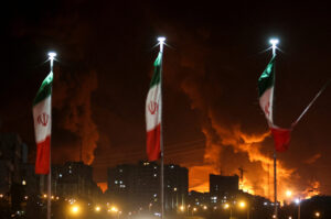 Banderas iraníes ondean mientras se eleva el fuego y el humo de un ataque israelí al depósito de petróleo de Sharan, tras los ataques israelíes contra Irán, en Teherán, Irán, el 15 de junio de 2025. Majid Asgaripour/WANA (Agencia de Noticias de Asia Occidental) vía