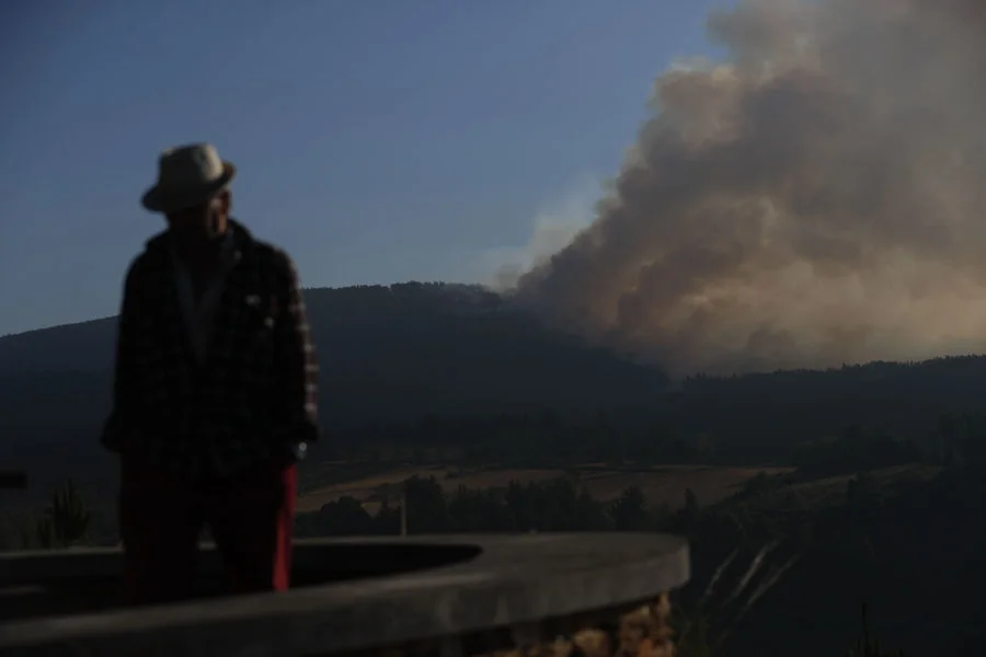 Un hombre camina con la columna de humo de fondo desde el Mirador da Capela en Pobra de Brollón, Lugo. Imagen EFE