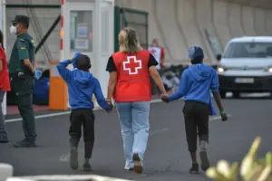 Un efectivo de la Cruz Roja escolta a dos de los menores trasladados en septiembre de 2023 junto a otros 313 migrantes desde el puerto de La Estaca en El Hierro, a la isla de Tenerife. EFE/Gelmert Finol