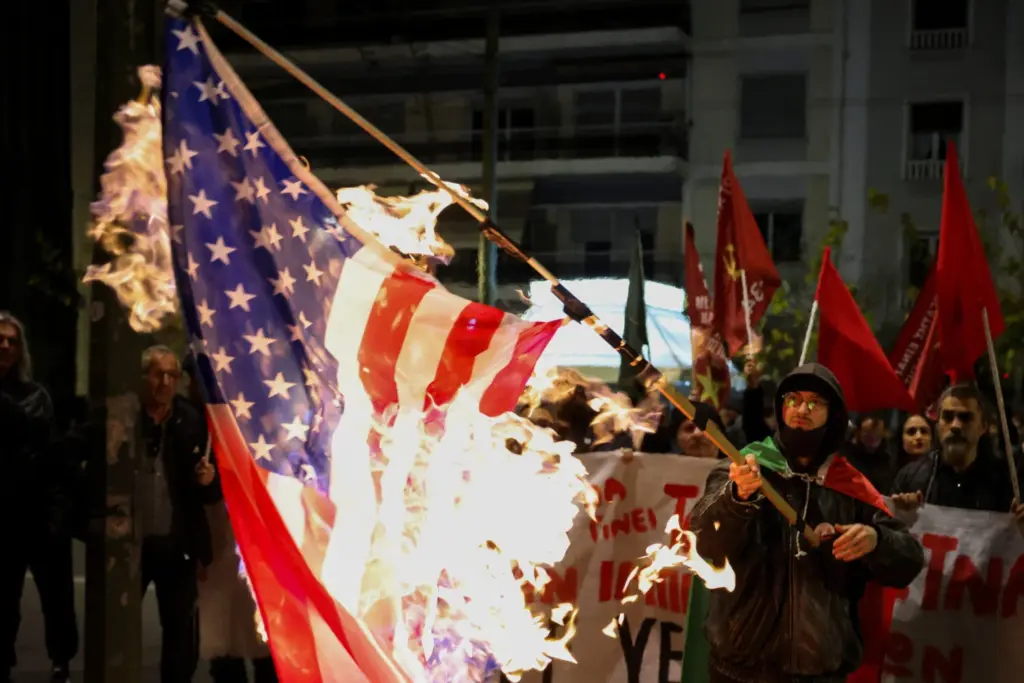 Un hombre sostiene una bandera estadounidense en llamas, mientras la gente, incluidos miembros del Partido Comunista Griego (KKE), se manifiesta contra la captura del presidente venezolano Nicolás Maduro, luego de que Estados Unidos atacara a Venezuela y capturara al presidente Maduro, afuera de la Embajada de Estados Unidos, en Atenas, Grecia, el 3 de enero de 2026. REUTERS/Louiza Vradi