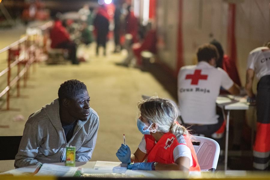 Uno de los 39 supervivientes de la lancha neumática rescatada este domingo al sur de Fuerteventura por Salvamento Marítimo conversa con una voluntaria de Cruz Roja al llegar al puerto de Gran Tarajal. Los ocupantes de esa zódiac han alertado este lunes de que parte de sus compañeros murieron antes de que les encontraran. Según la ONG Caminando Fronteras, son doce los desaparecidos, entre ellos tres mujeres. EFE/Carlos de Saá
