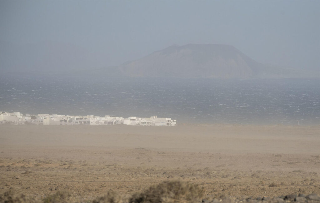 Una masa de aire cargada de polvo del Sahara envuelve Canarias tras el paso de la borrasca Dorothea, reduciendo la visibilidad en algunos casos por debajo de mil metros. En la imagen, la isla de La Graciosa apenas se intuye tras la calima desde la playa de Famara. EFE